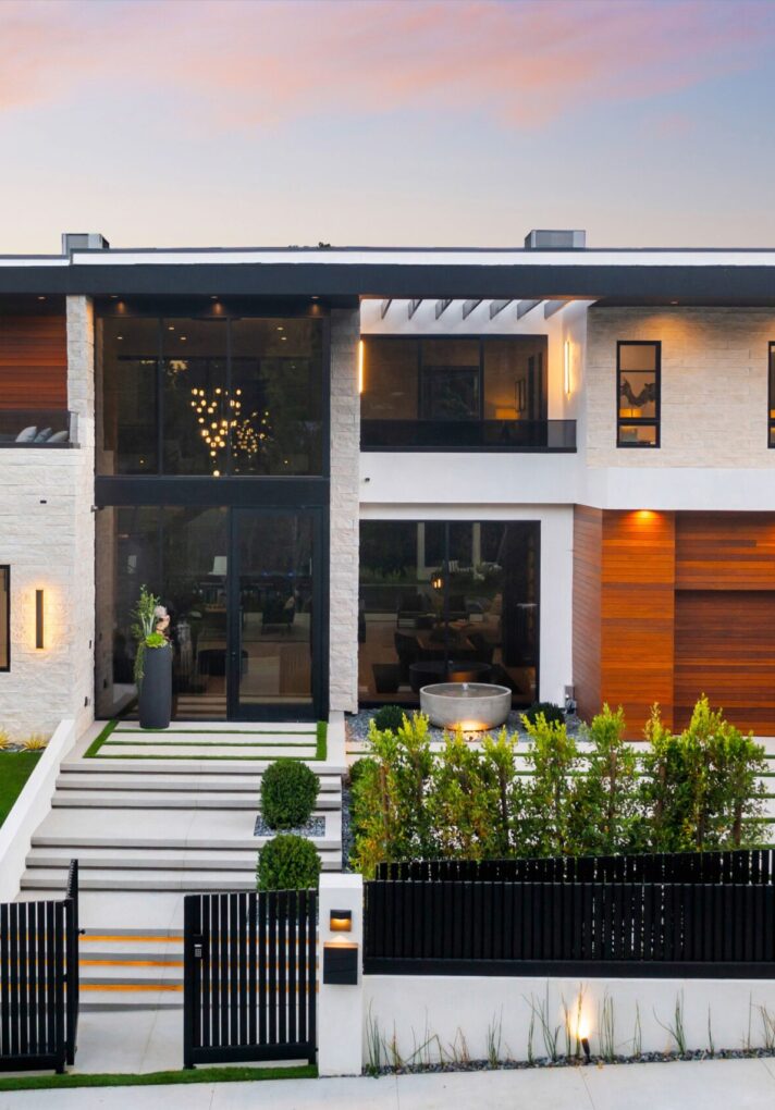 A modern luxury house with large windows, a manicured lawn, and a sunset sky in the background.